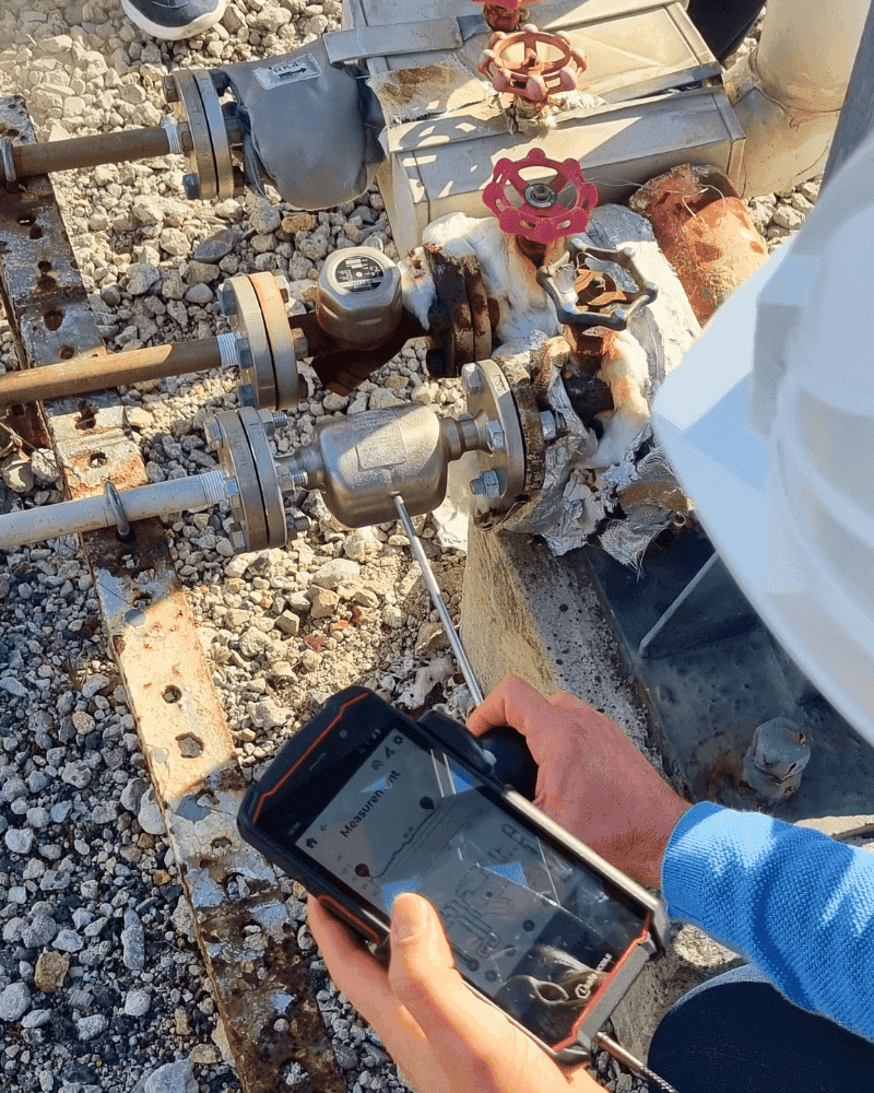 Hände halten ein robustes Smartphone mit Messbildschirm, der Wellenleiter liegt an einem isolierten Ableiter an