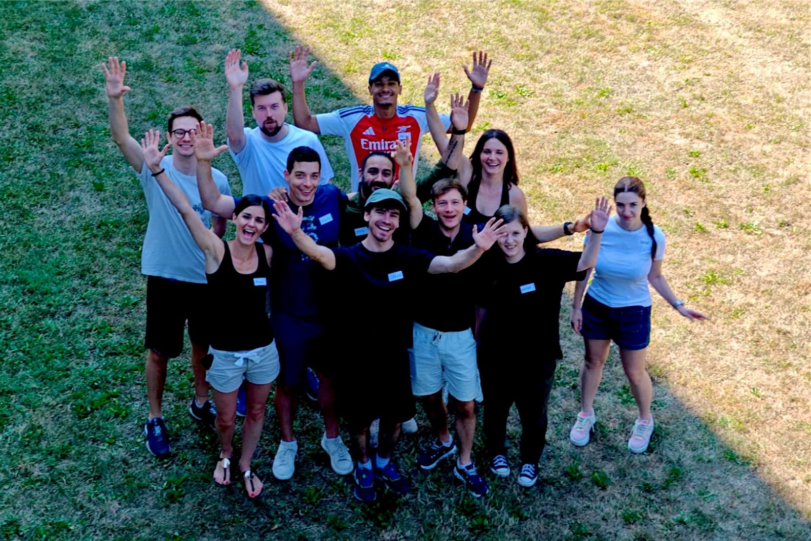 Das Senseven-Team steht auf einer Wiese und winkt in die Kamera, von oben fotografiert