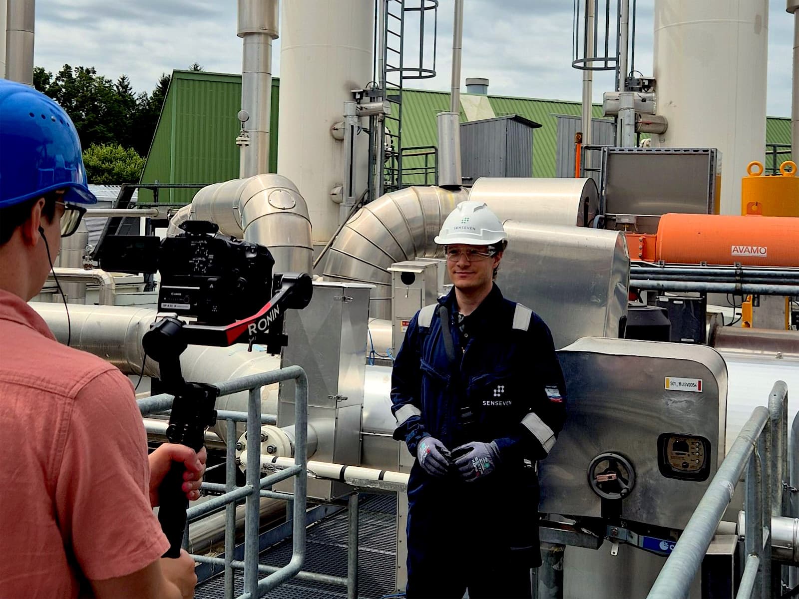 Camera operator filming a Senseven team member in protective gear at an industrial plant
