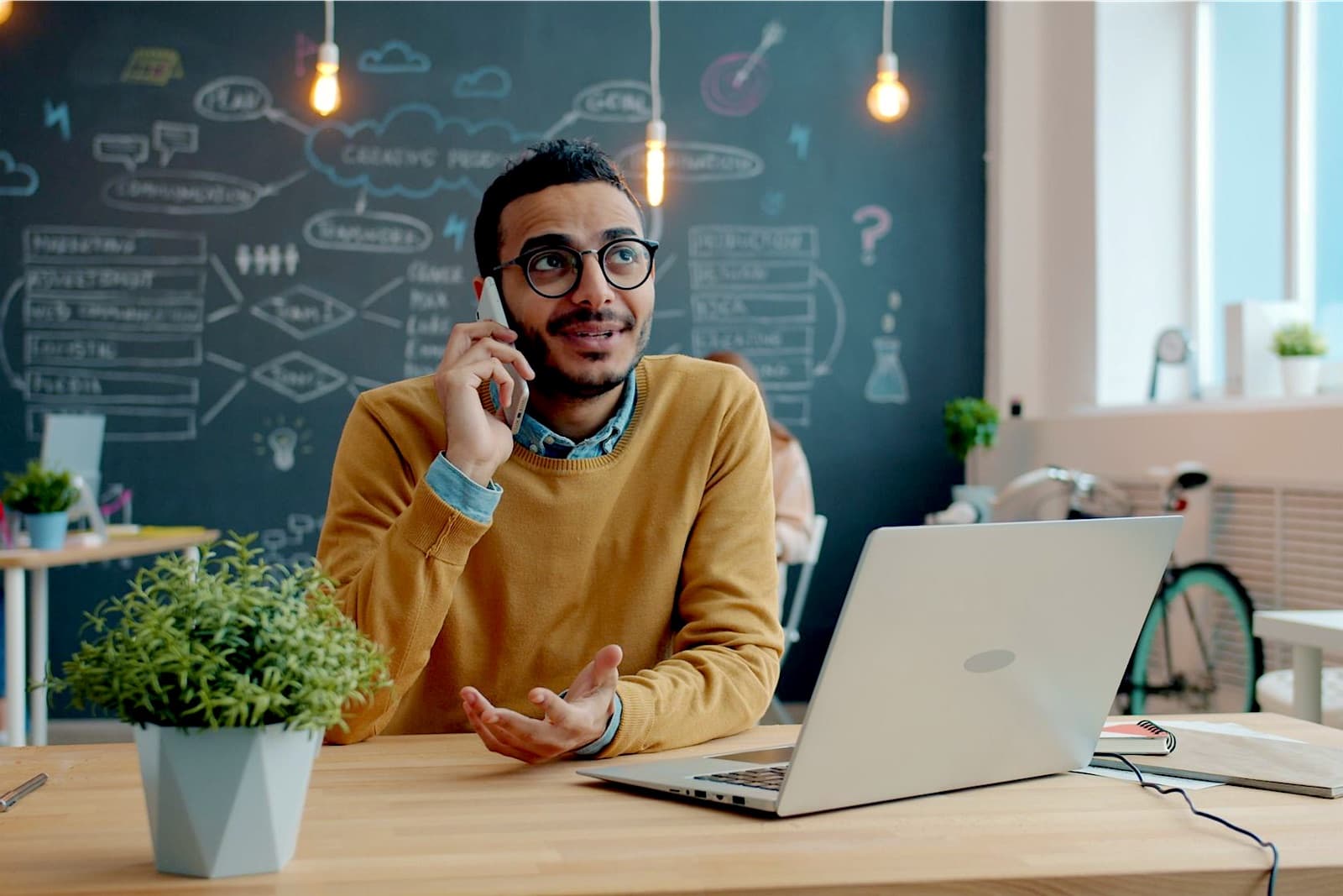 Junger Mann telefoniert lachend am Laptop in einem Startup-Büro mit Kreidewand
